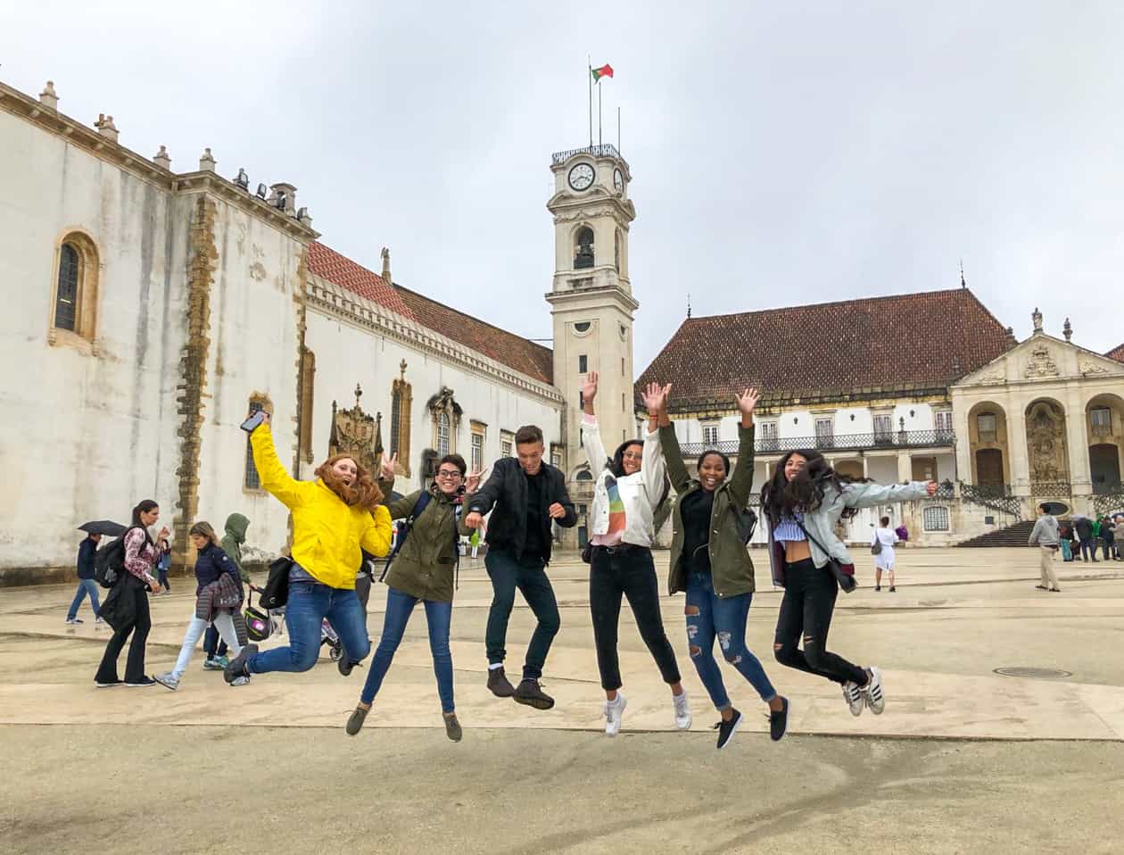 Students jumping in front of a building with a tower.