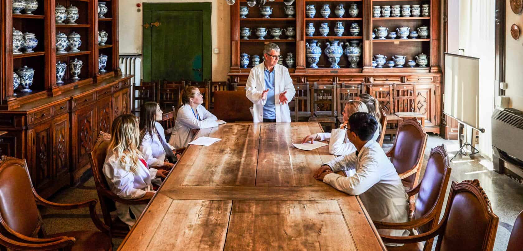 Students sitting around a table listening to a doctor.